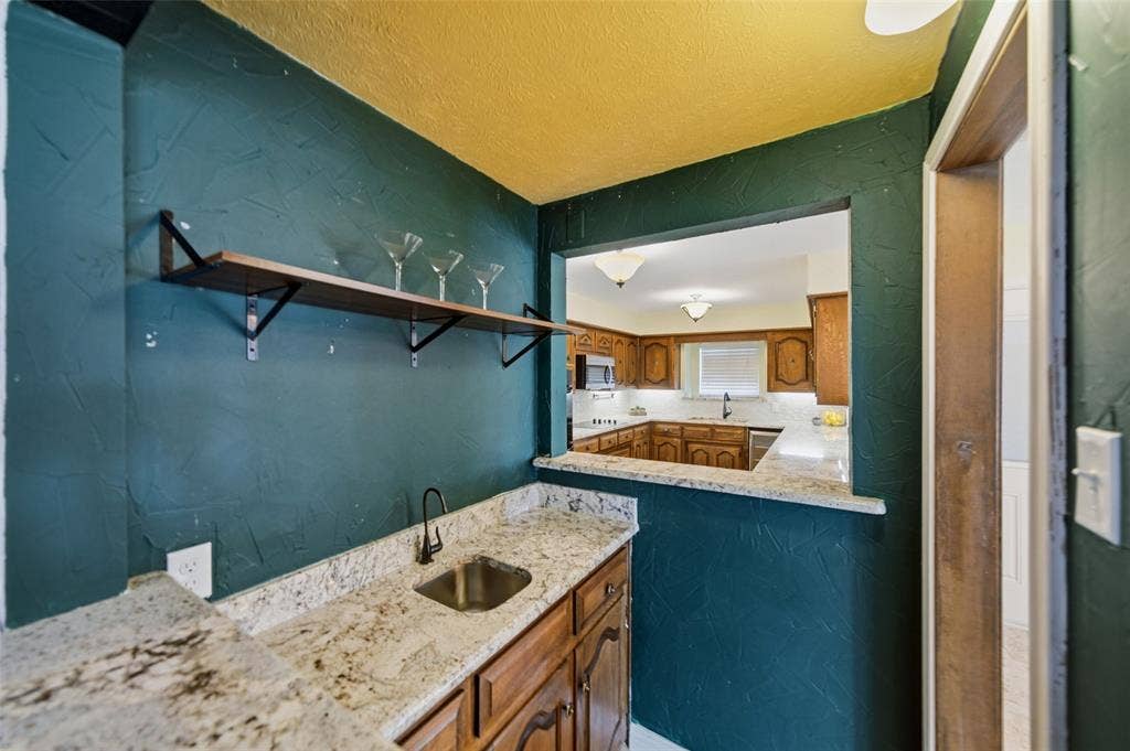 467 Harvest Glen Drive, Richardson, TX 75081 Built-in wet bar featuring stone countertops, a stainless steel undermount sink, a matte black gooseneck faucet, and open wood shelving.