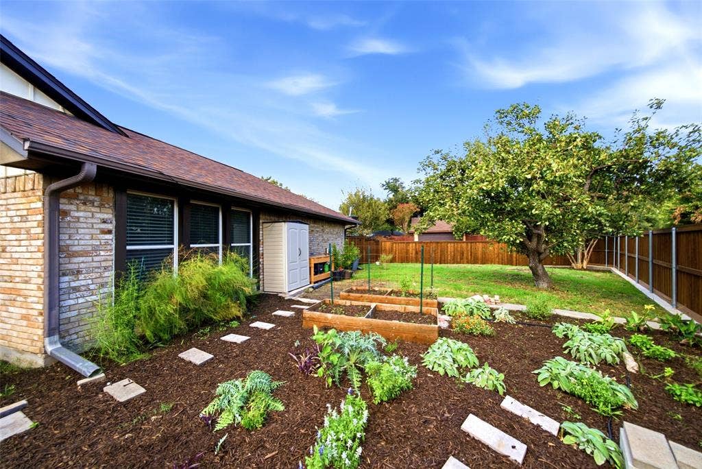 467 Harvest Glen Drive, Richardson, TX 75081 Backyard featuring raised garden beds, wood mulch ground cover, concrete paver pathway, mature tree, and wood privacy fencing