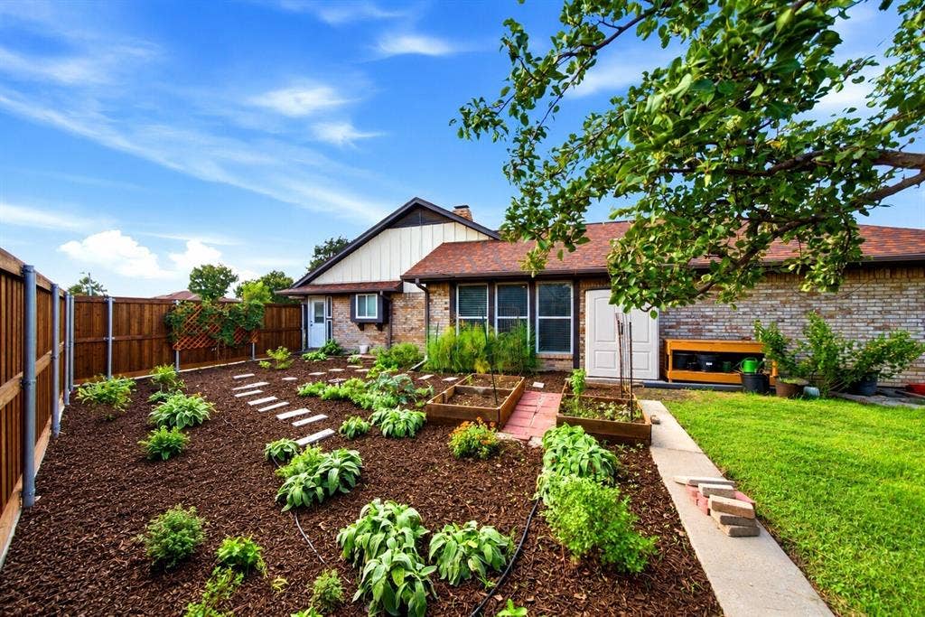 467 Harvest Glen Drive, Richardson, TX 75081 Backyard featuring elevated wood garden beds, stone paver pathway, wood privacy fencing, and brick exterior finish