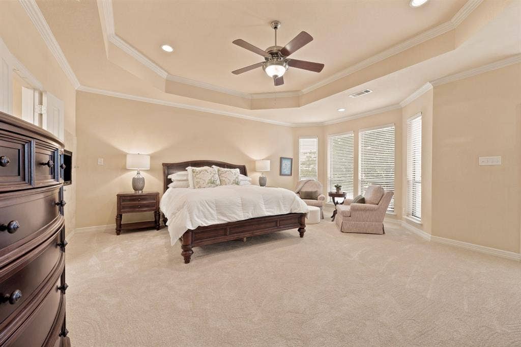 Spacious bedroom featuring plush carpeting, a tray ceiling with recessed lighting and a ceiling fan, and a bay window area with multiple windows