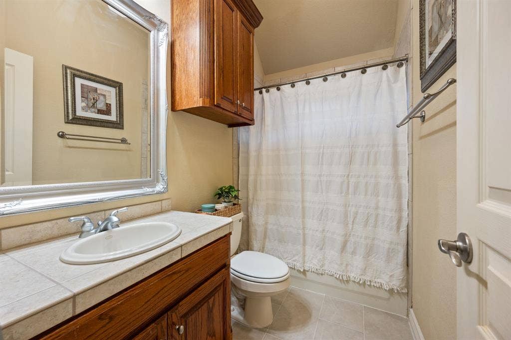 Bathroom featuring a tile-surround vanity with an integrated basin, stained wood cabinetry, a matching wall-mounted storage cabinet, and neutral tile flooring