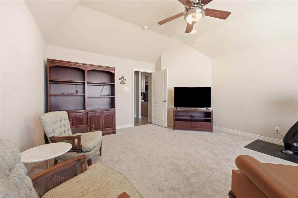 Vaulted ceilings featuring a central ceiling fan with integrated lighting, built-in floor-to-ceiling wooden shelving, and wall-to-wall carpeting