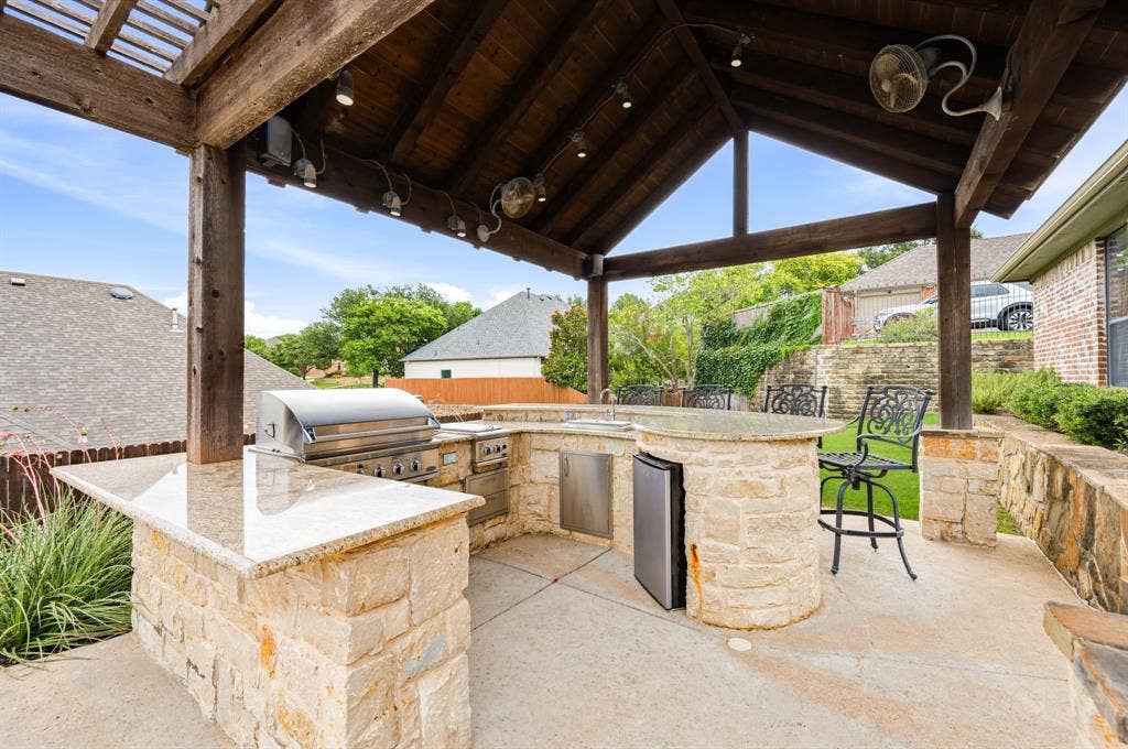 Covered outdoor kitchen featuring a built-in grill, integrated sink, and under-counter refrigerator