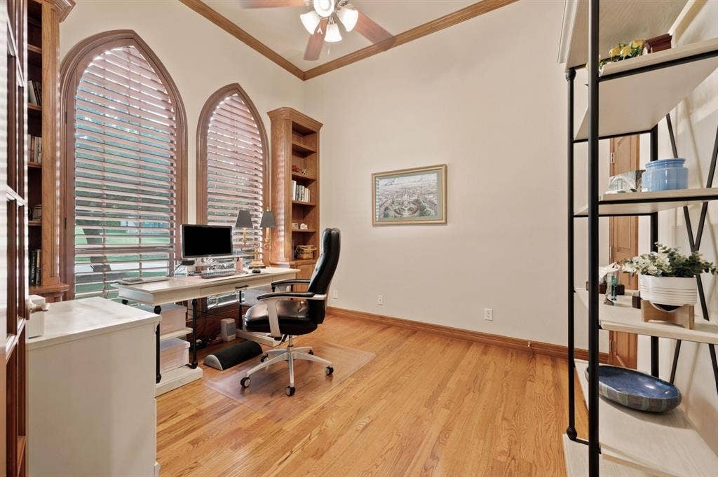 Spacious room featuring arched windows with wood frames and slatted blinds, hardwood flooring, and a ceiling fan