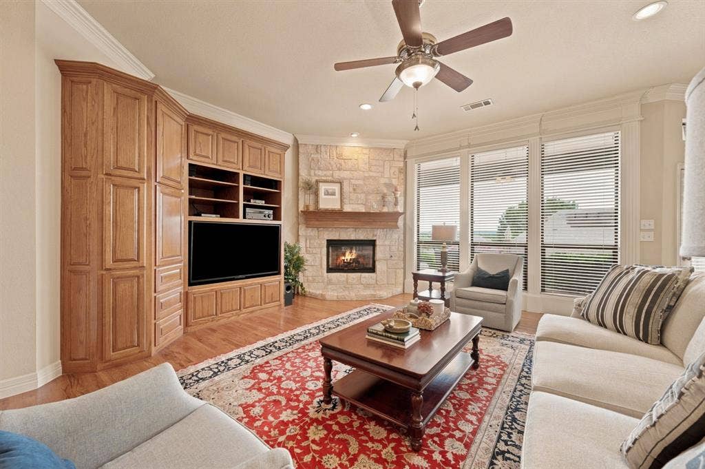 Hardwood flooring throughout featuring a corner stone fireplace with a wood mantle, built-in media cabinetry, and multiple windows with horizontal blinds