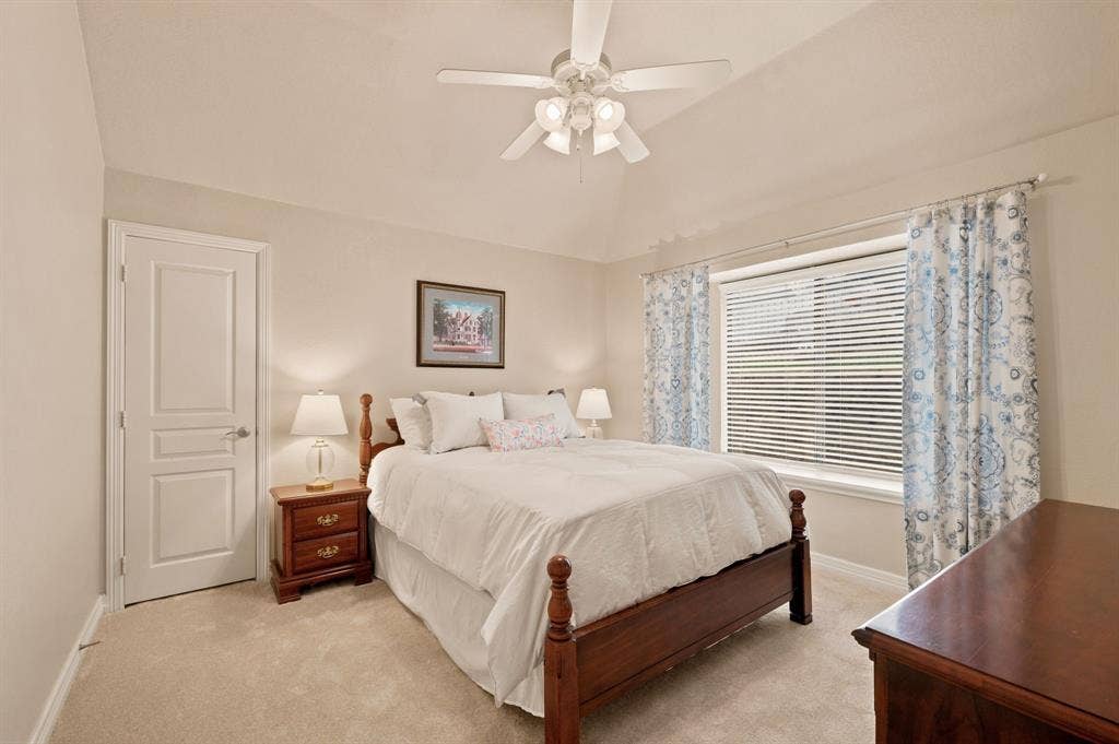 Vaulted ceiling bedroom featuring a ceiling fan, light neutral-toned carpeting, white trim, and a window with blinds