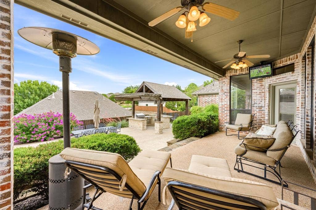 Covered patio featuring brick exterior, ceiling fans, and an outdoor television