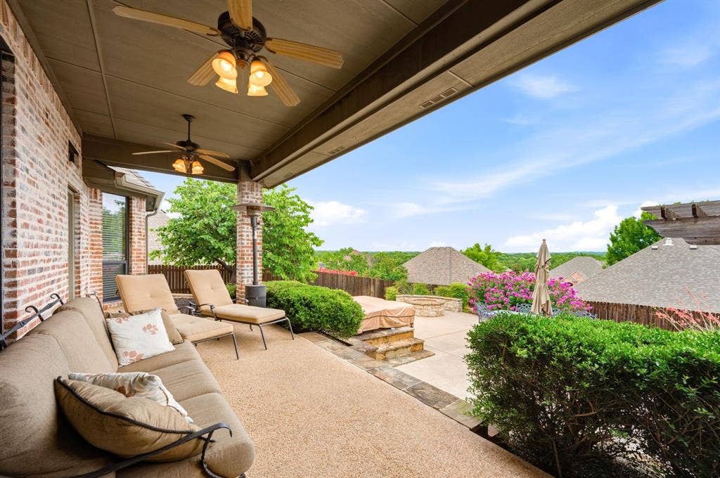 Covered patio featuring a textured concrete surface, brick exterior wall, and two ceiling fans with integrated lighting