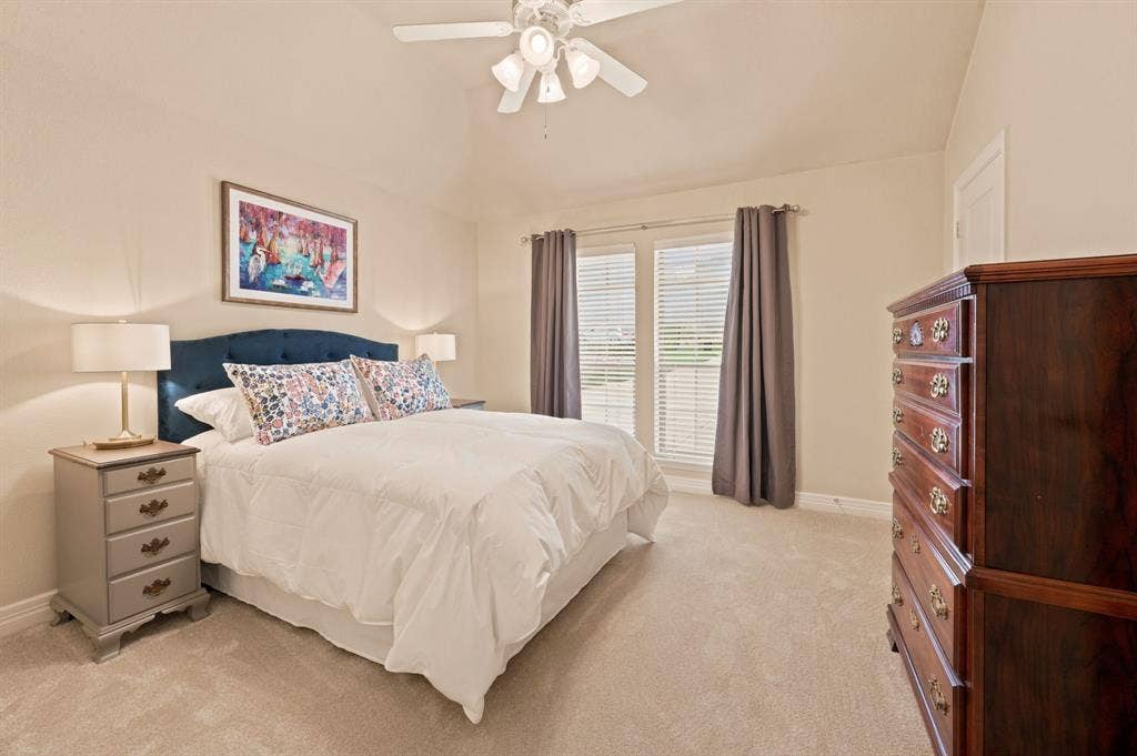 Vaulted ceiling bedroom with a ceiling fan, plush carpet flooring, and two large windows with blinds