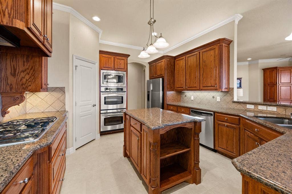 Kitchen featuring wood cabinetry, stone countertops, stainless steel double wall ovens, gas cooktop, and center island with built-in shelving