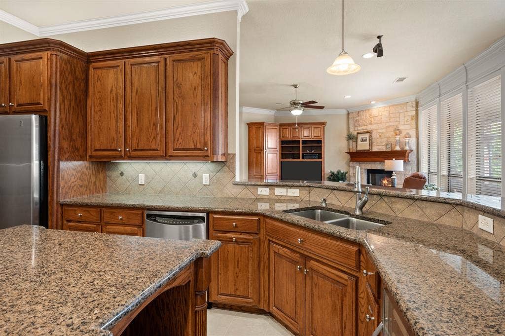 Kitchen featuring stained wood cabinetry, stone-finish countertops, diagonal tile backsplash, stainless steel dishwasher, and stone-faced fireplace with wood mantel