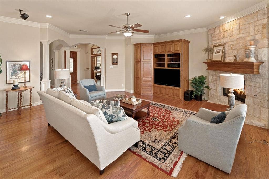 Living space featuring wood-finish flooring, a stone-clad fireplace with a substantial wood mantel, and built-in entertainment cabinetry