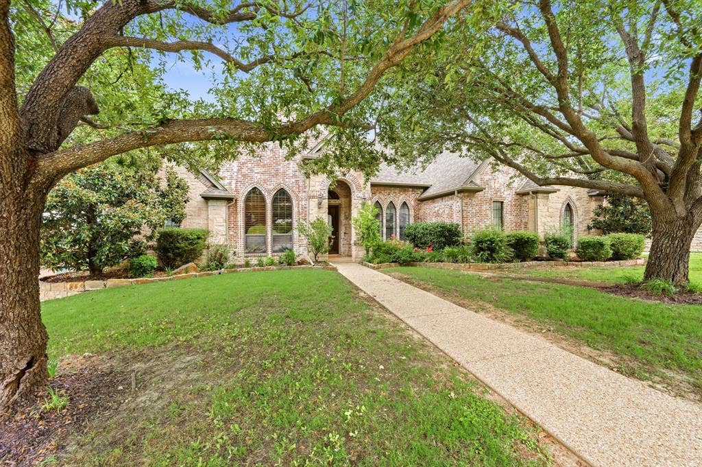 Brick and stone facade with arched windows, mature trees, and a textured pathway