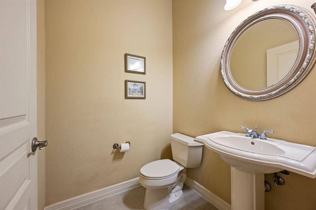 Pedestal sink with integrated basin, oval wall-mounted mirror, polished chrome dual-handle faucet, and ceramic toilet
