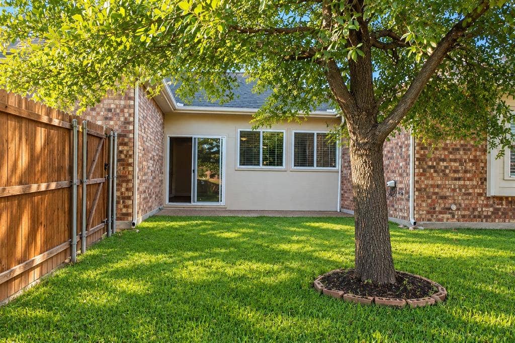 1731 Teakwood Drive, Wylie, TX 75098 Backyard space featuring brick exterior walls, a mature shade tree with a circular stone border, and a wood privacy fence