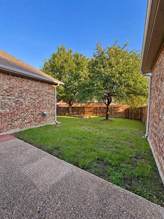 1731 Teakwood Drive, Wylie, TX 75098 Exterior brick facade, concrete patio, enclosed backyard with mature trees, and wooden perimeter fencing