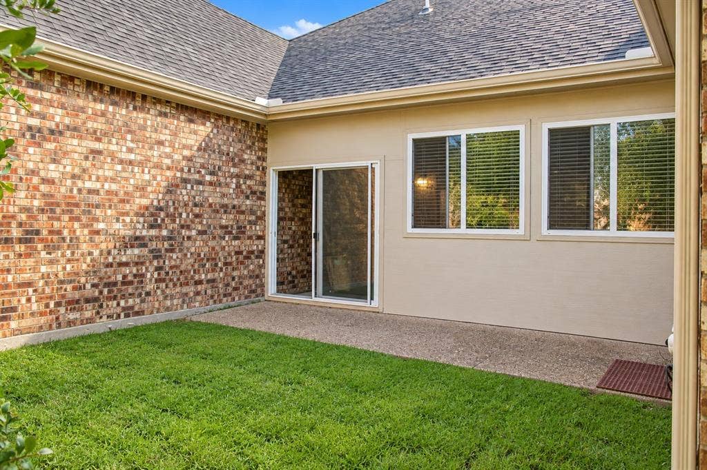 1731 Teakwood Drive, Wylie, TX 75098 Exterior side courtyard featuring a textured brick wall, concrete patio, grass lawn, and sliding glass door