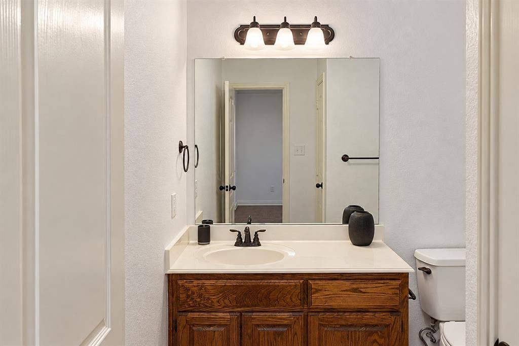 1731 Teakwood Drive, Wylie, TX 75098 Bathroom vanity featuring a wood-finish cabinet, integrated countertop with sink, wall-mounted light fixture, and framed mirror