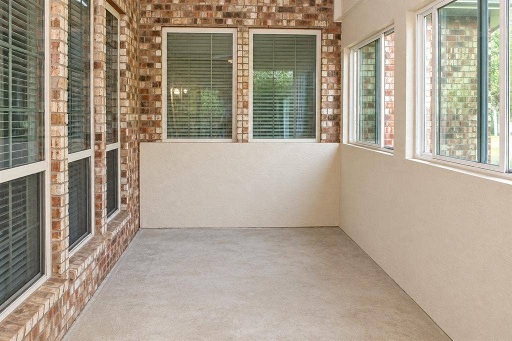 1731 Teakwood Drive, Wylie, TX 75098 Enclosed sunroom featuring exposed brick walls, multiple windows with integrated blinds, and concrete flooring