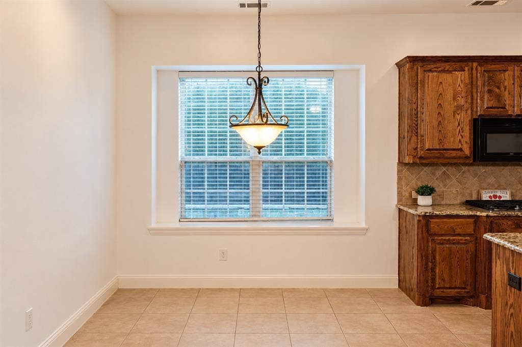 1731 Teakwood Drive, Wylie, TX 75098 Recessed window with paneled glass, stained wood cabinetry, stone-style countertop, diagonal tile backsplash, and decorative metal pendant lighting