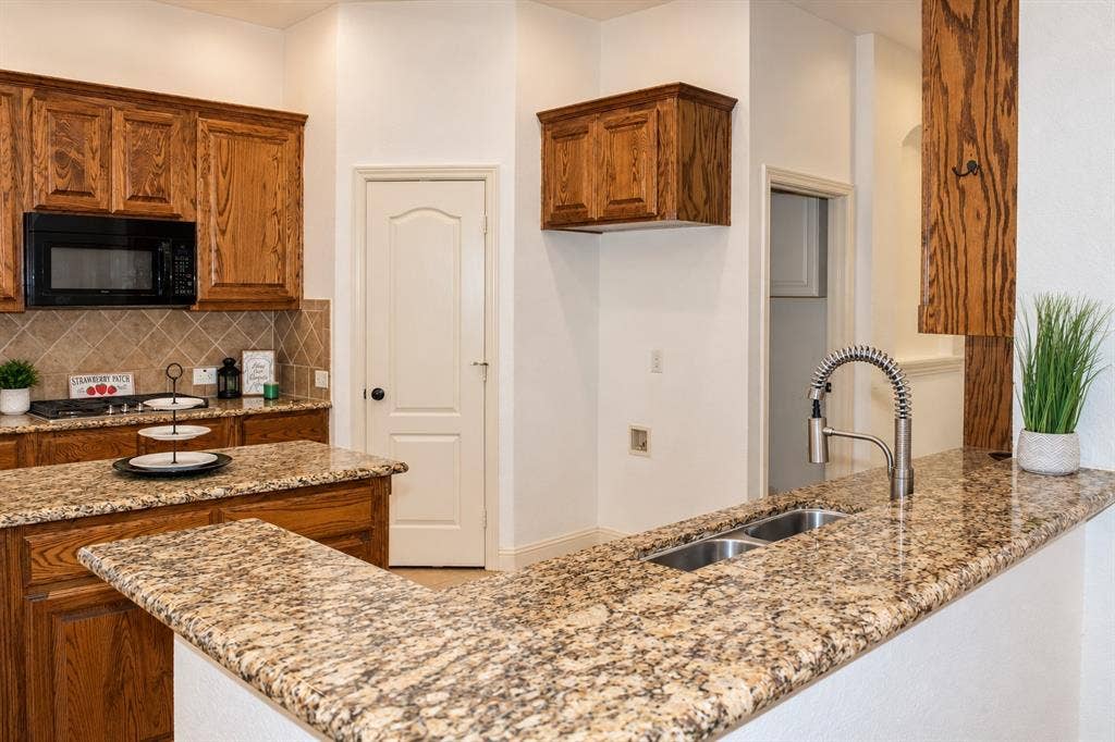 1731 Teakwood Drive, Wylie, TX 75098 Kitchen featuring medium-tone wood cabinetry, stone countertops, a double-basin stainless steel sink with a high-arch pull-down faucet, and a diagonal-set tile backsplash