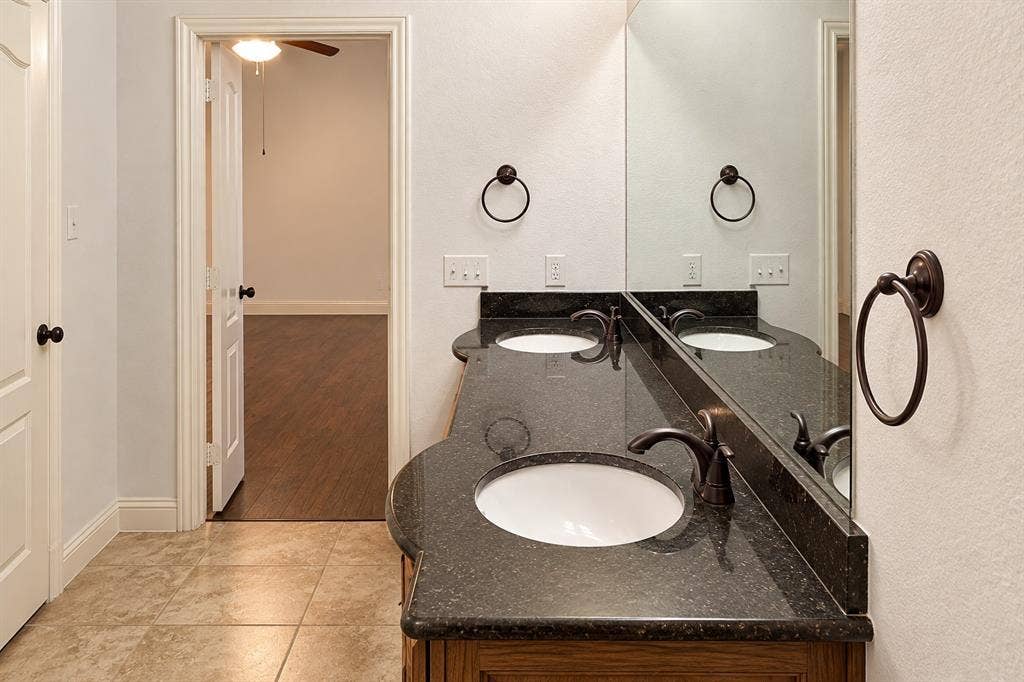 1731 Teakwood Drive, Wylie, TX 75098 Double vanity with dark stone countertop, undermount sinks, bronze-tone fixtures, and large plate-glass mirror