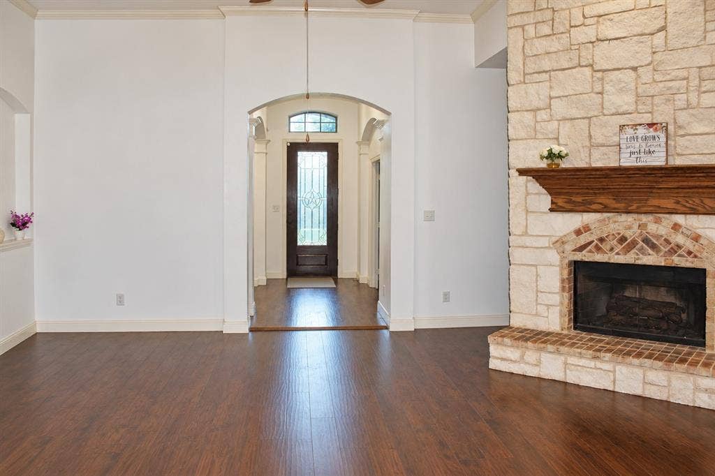 1731 Teakwood Drive, Wylie, TX 75098 Floor-to-ceiling stone fireplace featuring a wood mantel and brick hearth, dark wood-finish flooring, and arched entryway with decorative glass-panel door