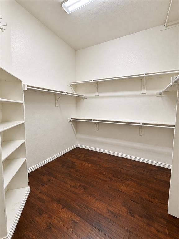 1731 Teakwood Drive, Wylie, TX 75098 Walk-in closet featuring dark wood-finish flooring, white built-in shelving, and multi-level wall-mounted rods