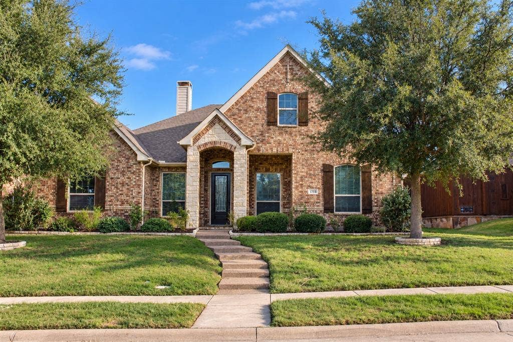1731 Teakwood Drive, Wylie, TX 75098 Brick exterior featuring a stone-accented arched entryway, wooden shutters, a chimney, and a concrete walkway