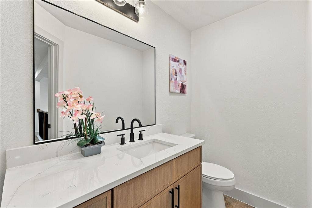5609 Hillview Court, McKinney, TX 75072 Vanity featuring a light wood-finish cabinet, white surface with veining, and a black-framed rectangular mirror, accented by a matte black faucet and multi-bulb industrial-style lighting