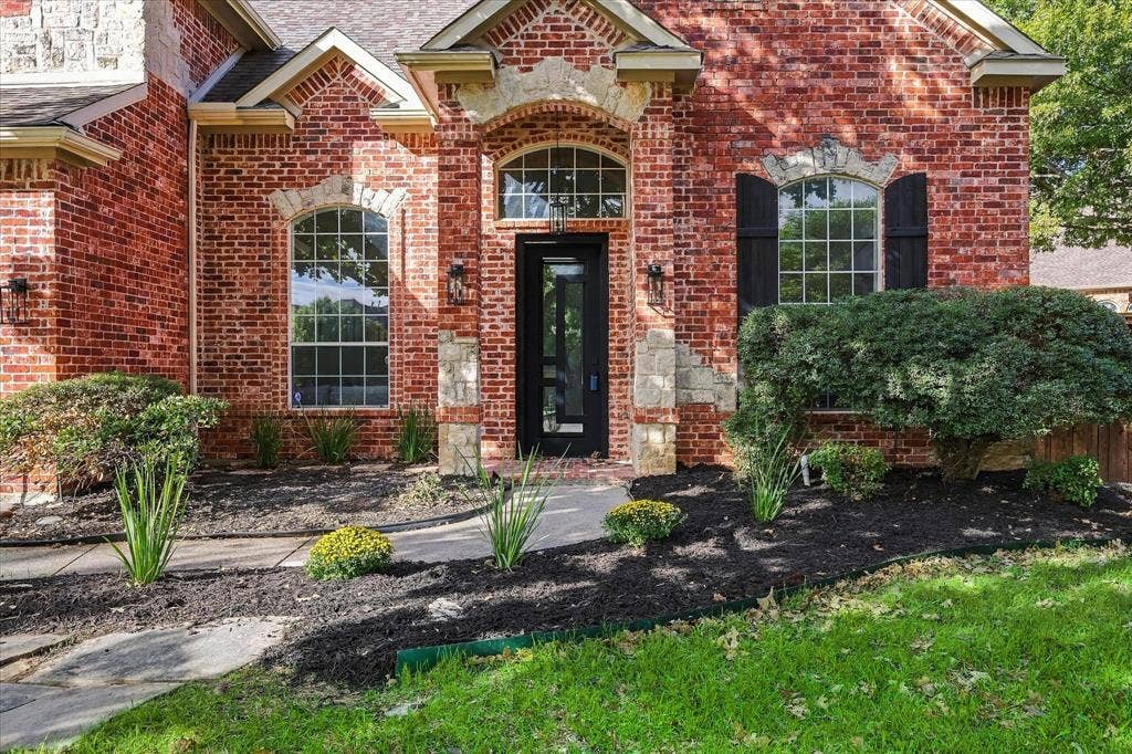 5609 Hillview Court, McKinney, TX 75072 Brick exterior featuring arched windows, stone masonry accents, black decorative shutters, and a covered entryway