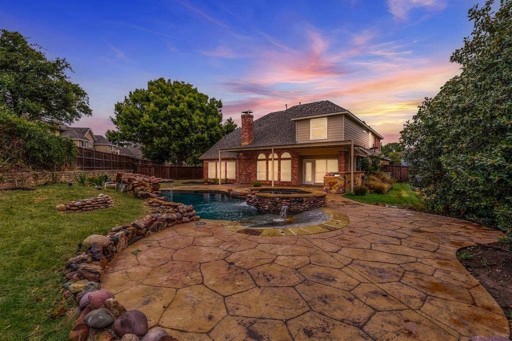 5609 Hillview Court, McKinney, TX 75072 Rear exterior featuring a brick and siding facade, covered patio, stone-accented pool with integrated spa, and extensive flagstone hardscaping