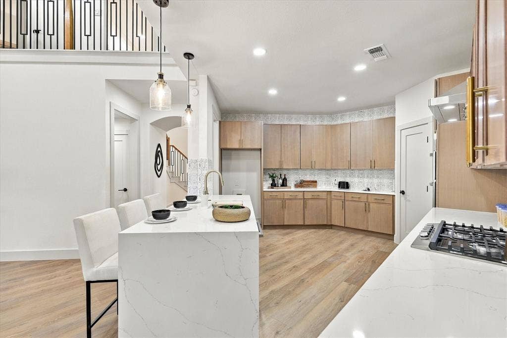 5609 Hillview Court, McKinney, TX 75072 Kitchen featuring a waterfall-edge island with stone-surface countertop, flat-panel light wood cabinetry, decorative patterned tile backsplash, recessed lighting, and wood-finish flooring