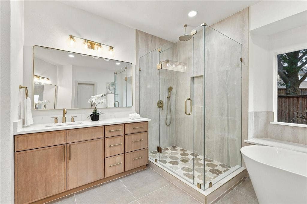 5609 Hillview Court, McKinney, TX 75072 Wood-finish vanity with countertop, glass-enclosed shower featuring patterned tile flooring, wall-mounted faucet, and freestanding soaking tub