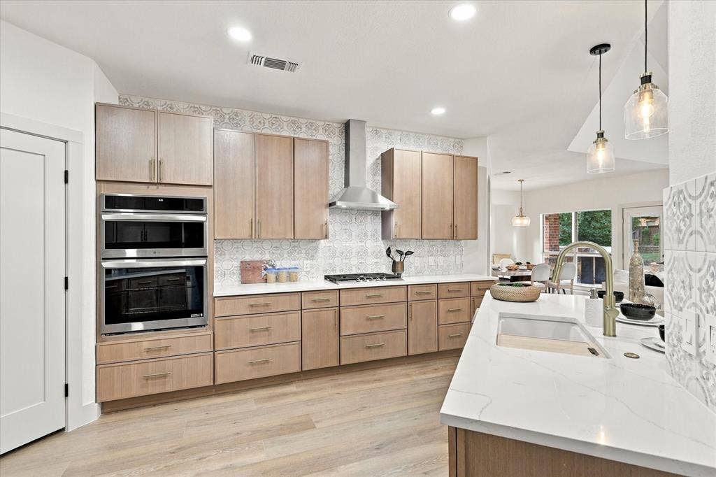 5609 Hillview Court, McKinney, TX 75072 Kitchen featuring light-finish cabinetry, white countertops with veining, patterned tile backsplash, stainless steel built-in double oven and range hood, and wood-finish flooring