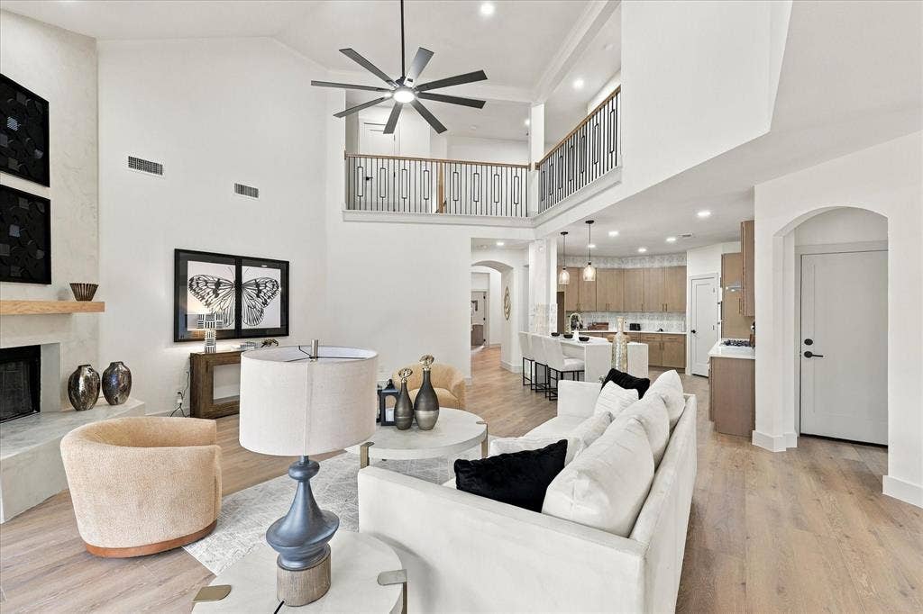 5609 Hillview Court, McKinney, TX 75072 Double-height living area featuring a vaulted ceiling, wood-finish flooring, a fireplace with a light-tone hearth and wood mantel, a multi-blade ceiling fan, and a metal balcony railing