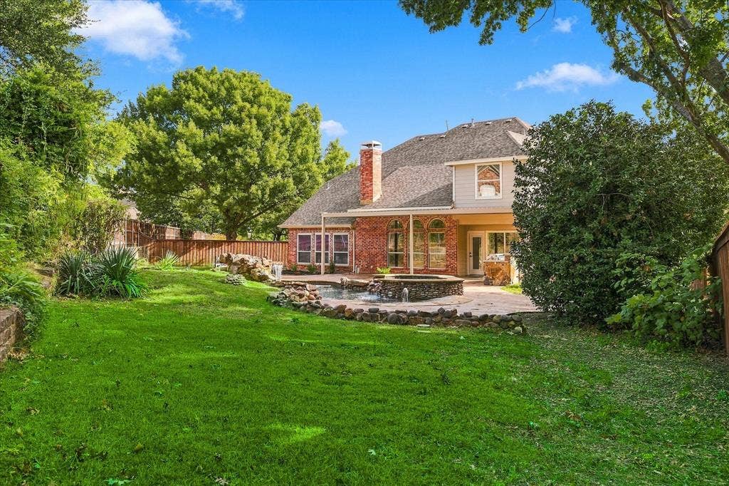 5609 Hillview Court, McKinney, TX 75072 Backyard featuring a brick and siding exterior, stone-accented spa, concrete patio, and mature trees enclosed by a wooden privacy fence