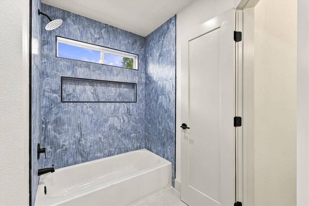 5609 Hillview Court, McKinney, TX 75072 Bathtub surround featuring blue patterned tile, matte black fixtures, an integrated wall niche, and a transom window