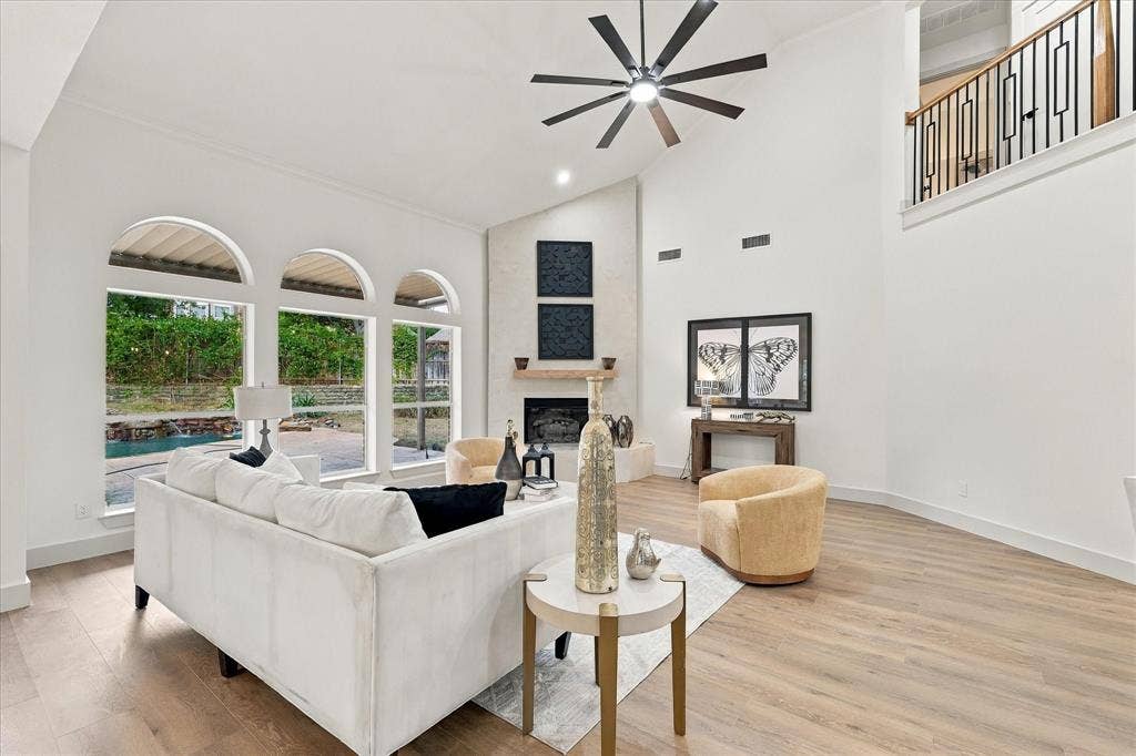 5609 Hillview Court, McKinney, TX 75072 Vaulted ceilings with a multi-blade ceiling fan, expansive arched windows, wood-finish flooring, and a fireplace with a stone-surround facade featuring a wooden mantel