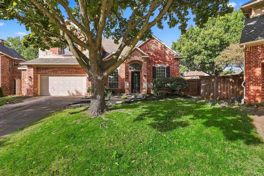 5609 Hillview Court, McKinney, TX 75072 Red brick exterior featuring a multi-gabled roofline, arched entryway, attached two-car garage, mature landscaping, and wood privacy fencing