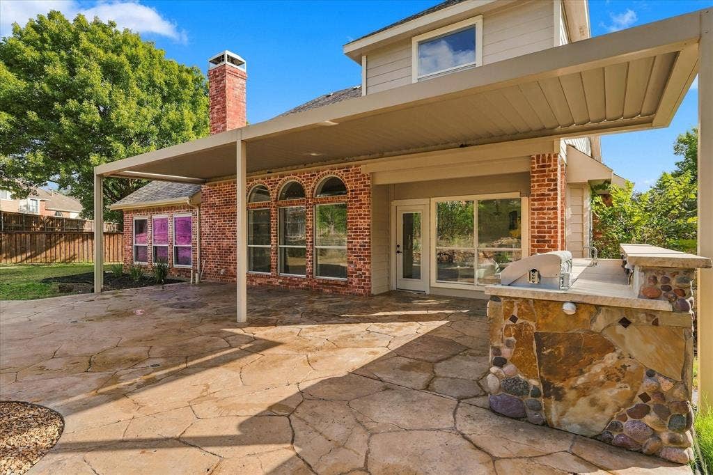 5609 Hillview Court, McKinney, TX 75072 Rear patio featuring flagstone paving, a covered pergola, built-in stone grill station, brick chimney, and arched windows