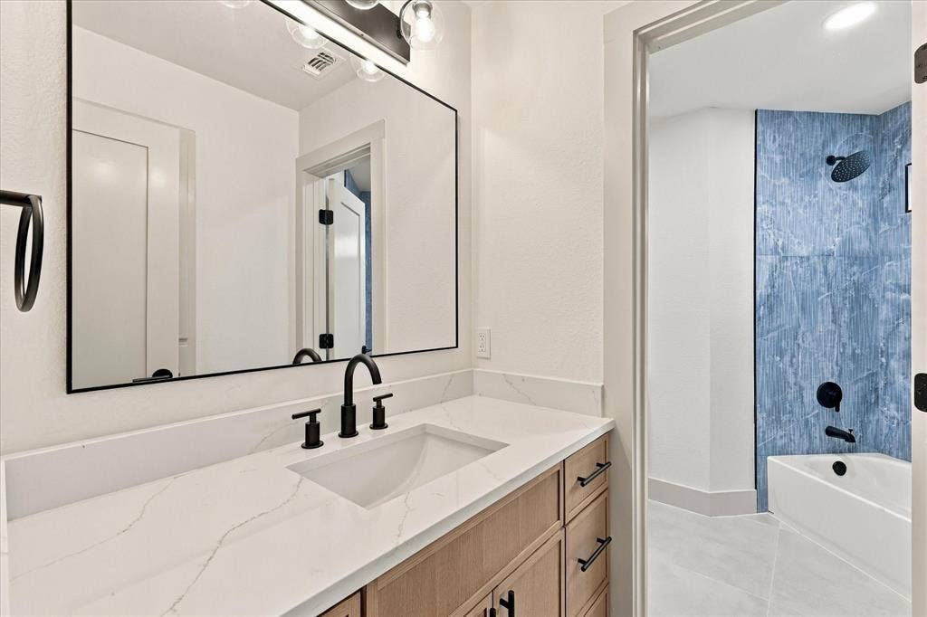 5609 Hillview Court, McKinney, TX 75072 Bathroom featuring a vanity with a white stone-look countertop, wood-finish cabinetry, a large rectangular mirror, and matte black hardware including a wall-mounted light fixture and widespread faucet