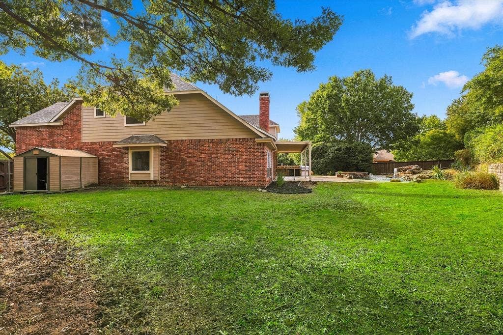 5609 Hillview Court, McKinney, TX 75072 Expansive backyard featuring a brick and siding exterior, a masonry chimney, a covered patio, and a stone-accented water feature