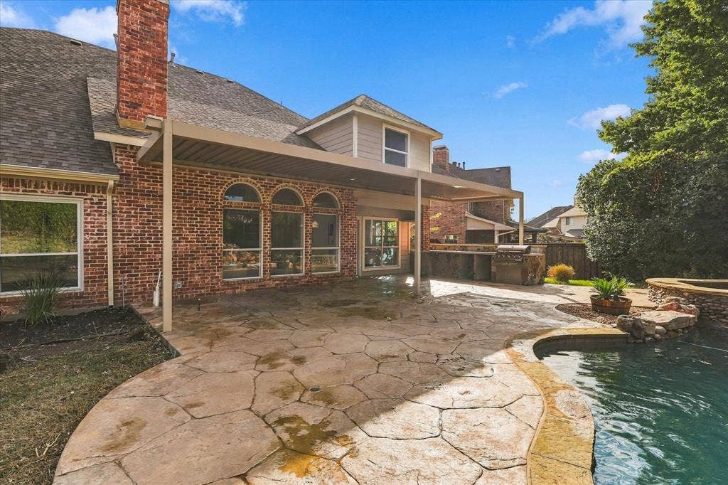 5609 Hillview Court, McKinney, TX 75072 Brick exterior with arched windows, covered patio, outdoor kitchen with stone finish, and swimming pool