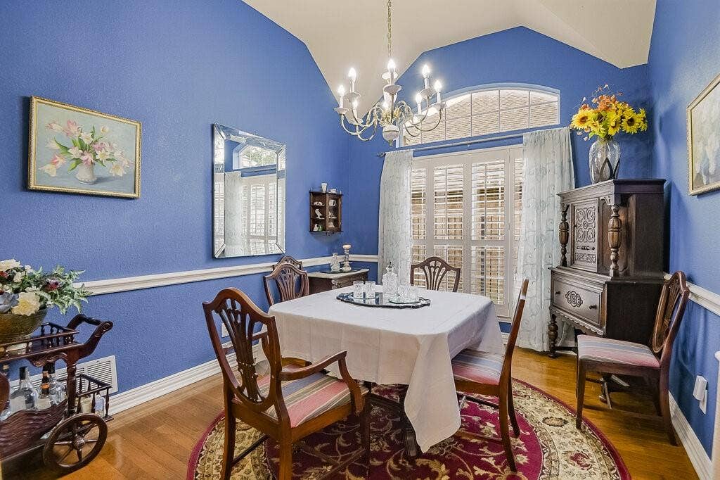 Elegant dining room with large window, wood floors, and plantation shutters.
