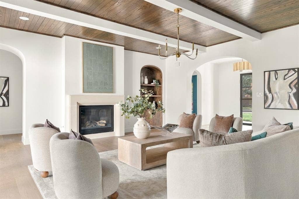 4953 Forest Bend Road, Dallas, TX 75244 Living area featuring a stained wood-finish coffered ceiling, arched doorways, a stone-surround fireplace, and custom arched built-in shelving