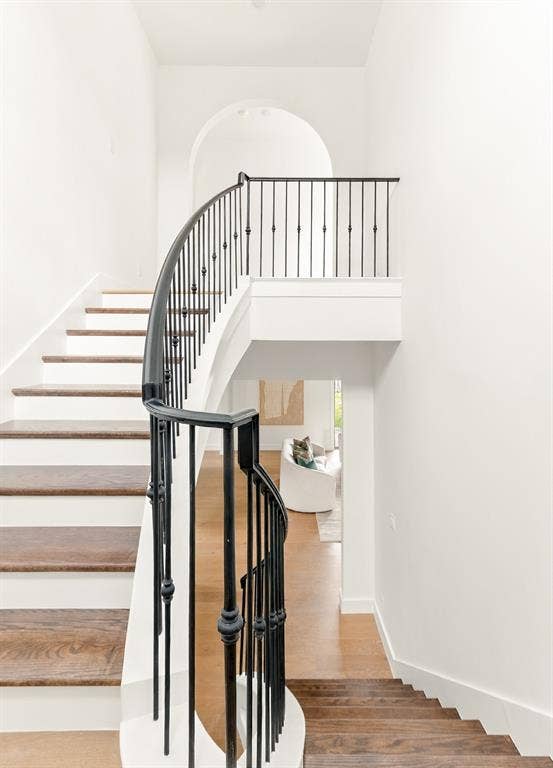 4953 Forest Bend Road, Dallas, TX 75244 Curved staircase featuring dark wood-finish treads, white risers, and black metal balusters topped with an arched architectural detail