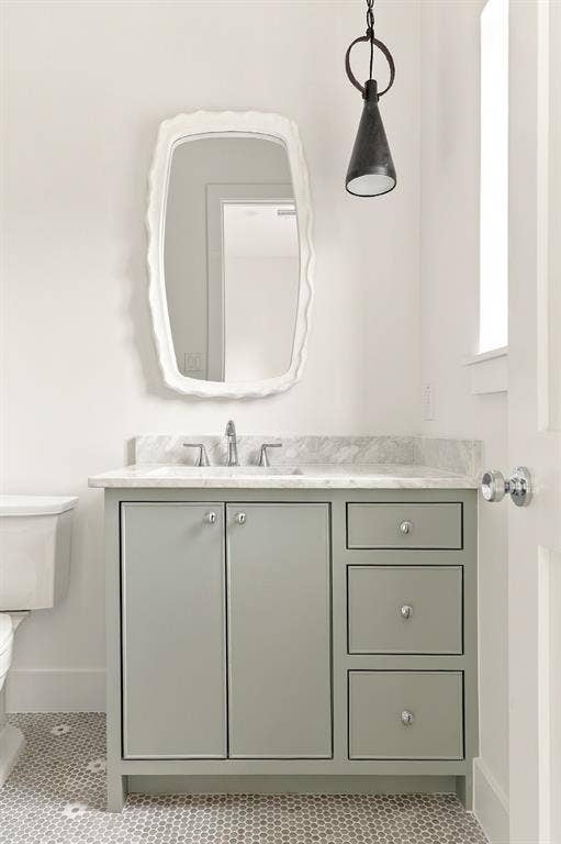 4953 Forest Bend Road, Dallas, TX 75244 Custom sage-toned vanity featuring a stone countertop, an integrated sink, polished hardware, a sculptural wall-mounted pendant light, and a geometric-patterned tile floor