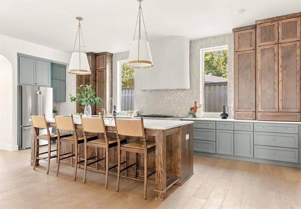 4953 Forest Bend Road, Dallas, TX 75244 Custom kitchen featuring a large central island with seating space, floor-to-ceiling wood cabinetry, a decorative range hood, stone-finish countertops, and wood-finish flooring