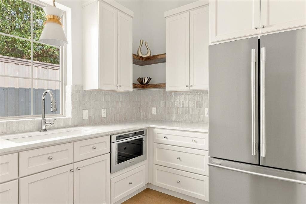 4953 Forest Bend Road, Dallas, TX 75244 Kitchen featuring white shaker-style cabinetry, a textured tile backsplash, built-in stainless steel oven, a farmhouse-style sink with a pull-down faucet, and floating wood corner shelving